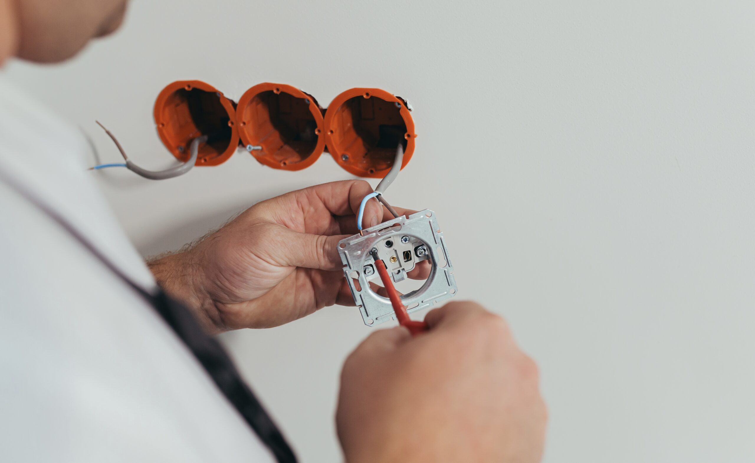 Male worker professional electrician mounts an electrical outlet in the apartment after repair, close-up photo of the installer